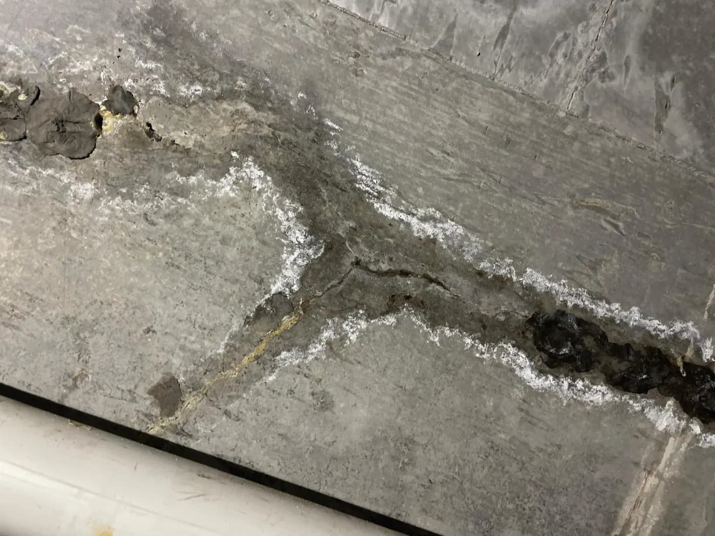 Concrete slab with a long crack lined with white crystallised salts and the concrete breaking away along its edges