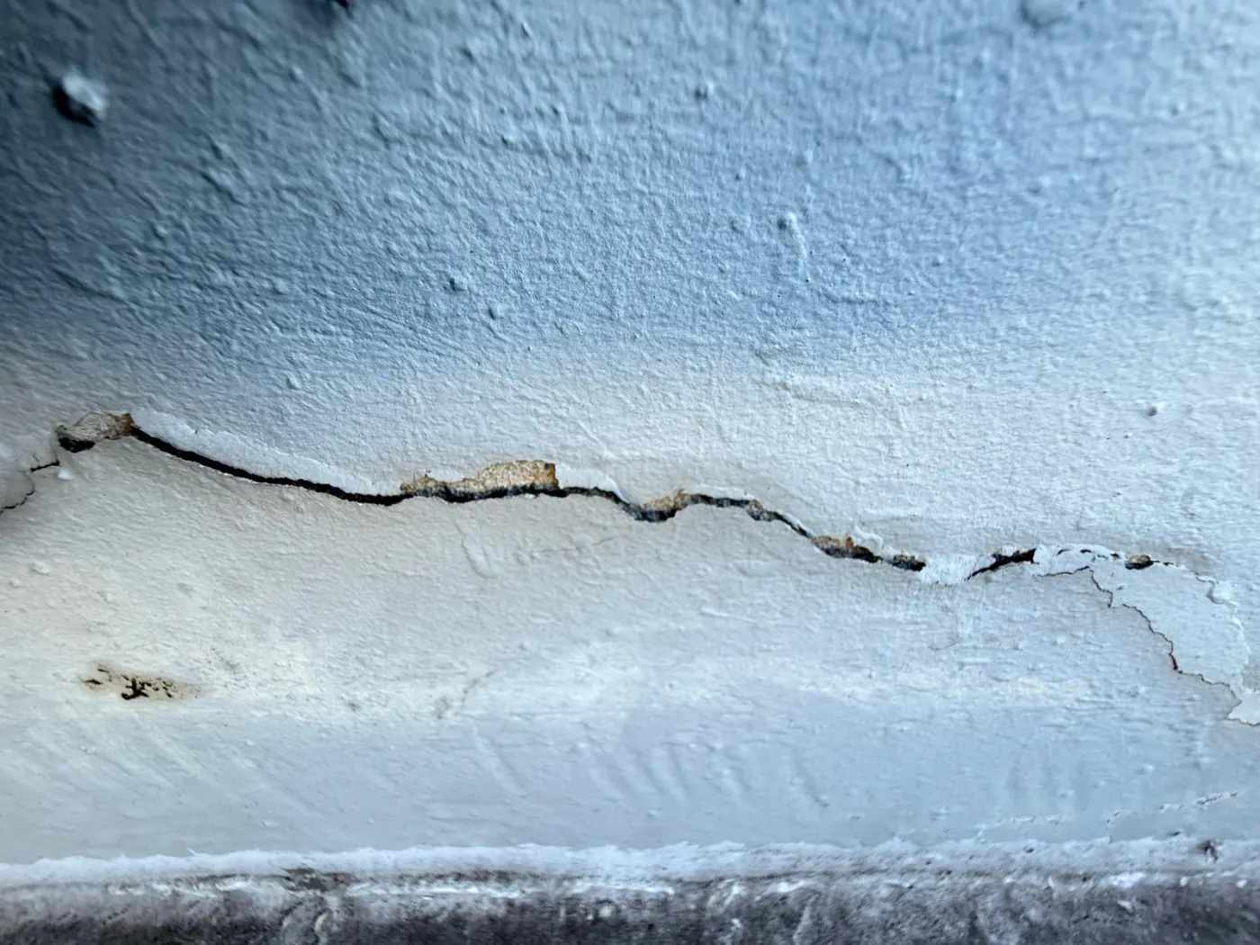 Painted rendered wall with a horizontal crack, the render lifting away from the substrate along it