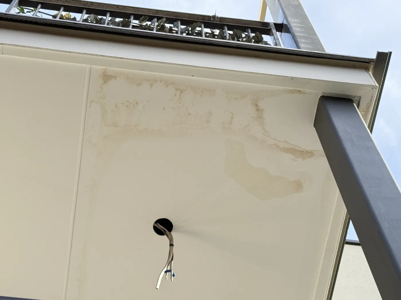 Underside of a balcony soffit with brown tide marks around a light fitting, the water coming through the slab from the balcony above